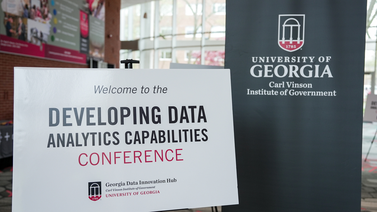 sign that says "Welcome to the Developing Data Analytics Capabilities Conference" beside a banner with the Institute of Government logo