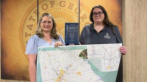 Project leads Angela Wheeler of the Institute of Government (right) and Kiisa Wiegand of GDOT with the map and the award.