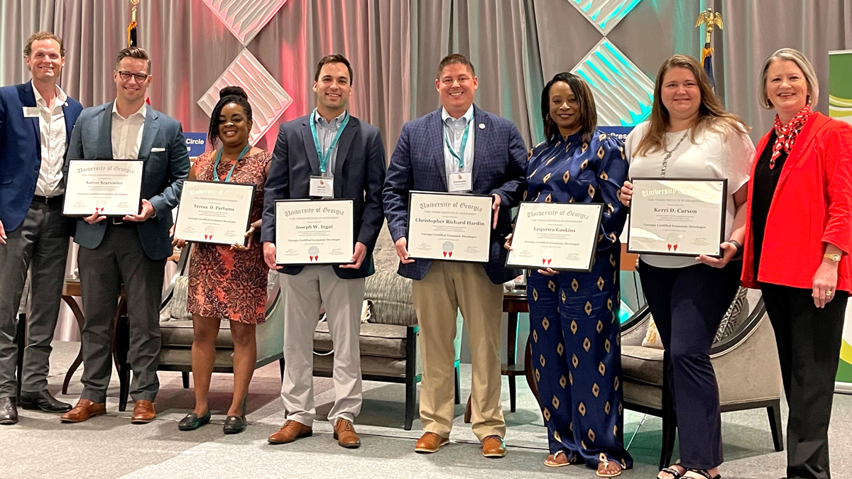 This image shows GCED graduates, holding their certificates, standing beside GEDA President & CEO Grant Cagle and Institute of Government faculty member Jennifer Nelson.