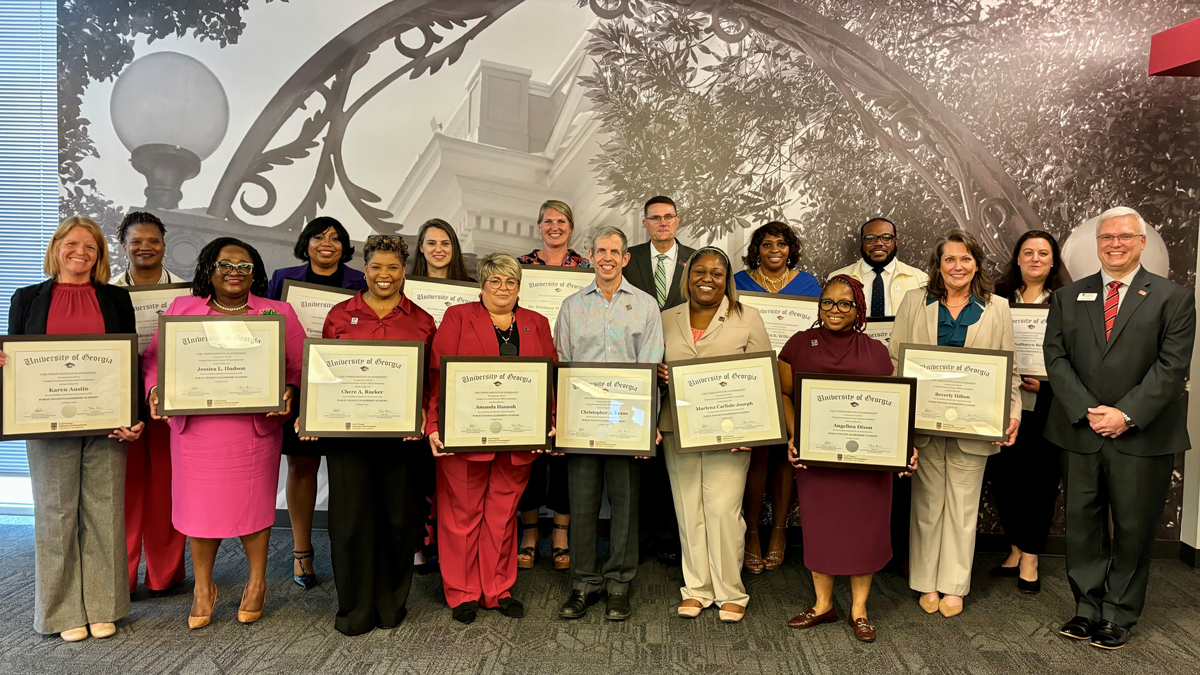 This image shows 16 graduates along with instructor John Hulsey. The graduates are holding their certificates.
